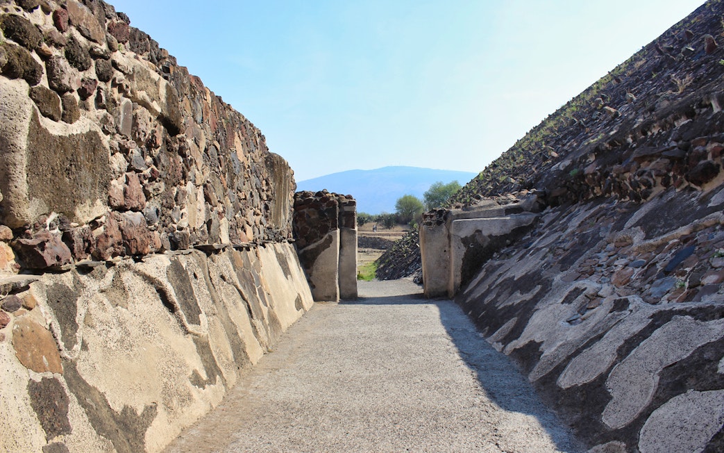 Teotihuacán Pyramid pathway with stone walls and distant mountain view.