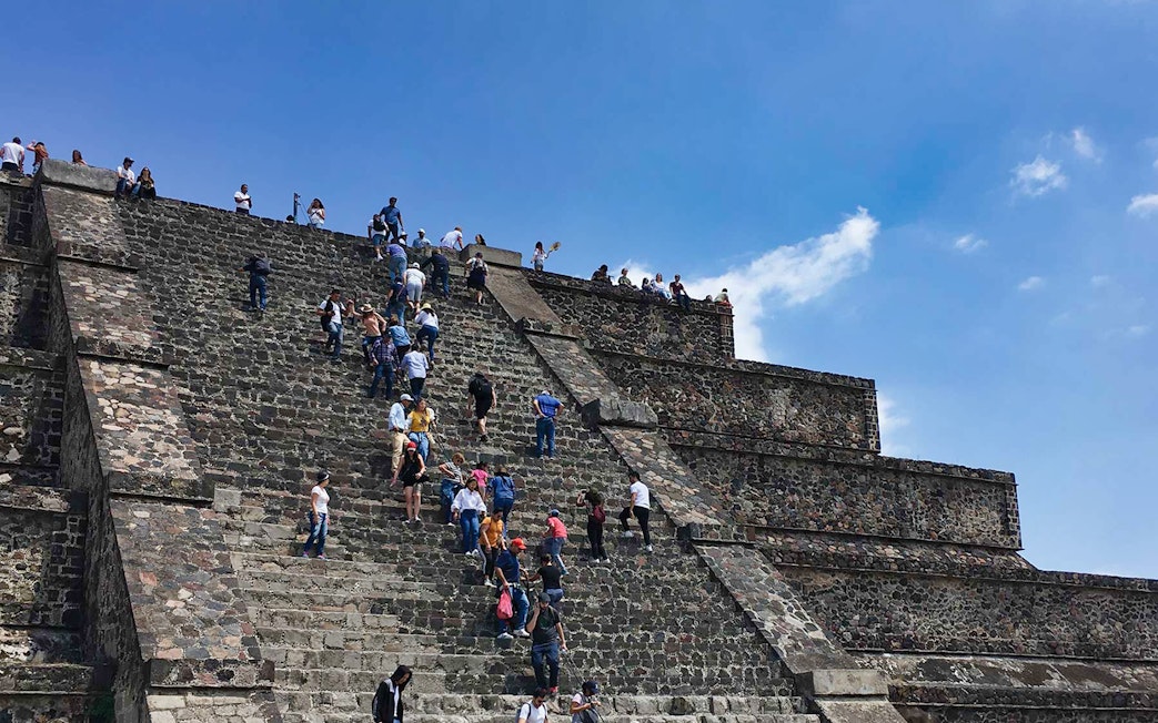 Visitors climbing the Teotihuacán Pyramid steps under a clear sky.