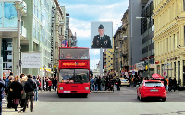 Hop-on hop-off bus at Checkpoint Charlie, Berlin, with tourists exploring the historic site.
