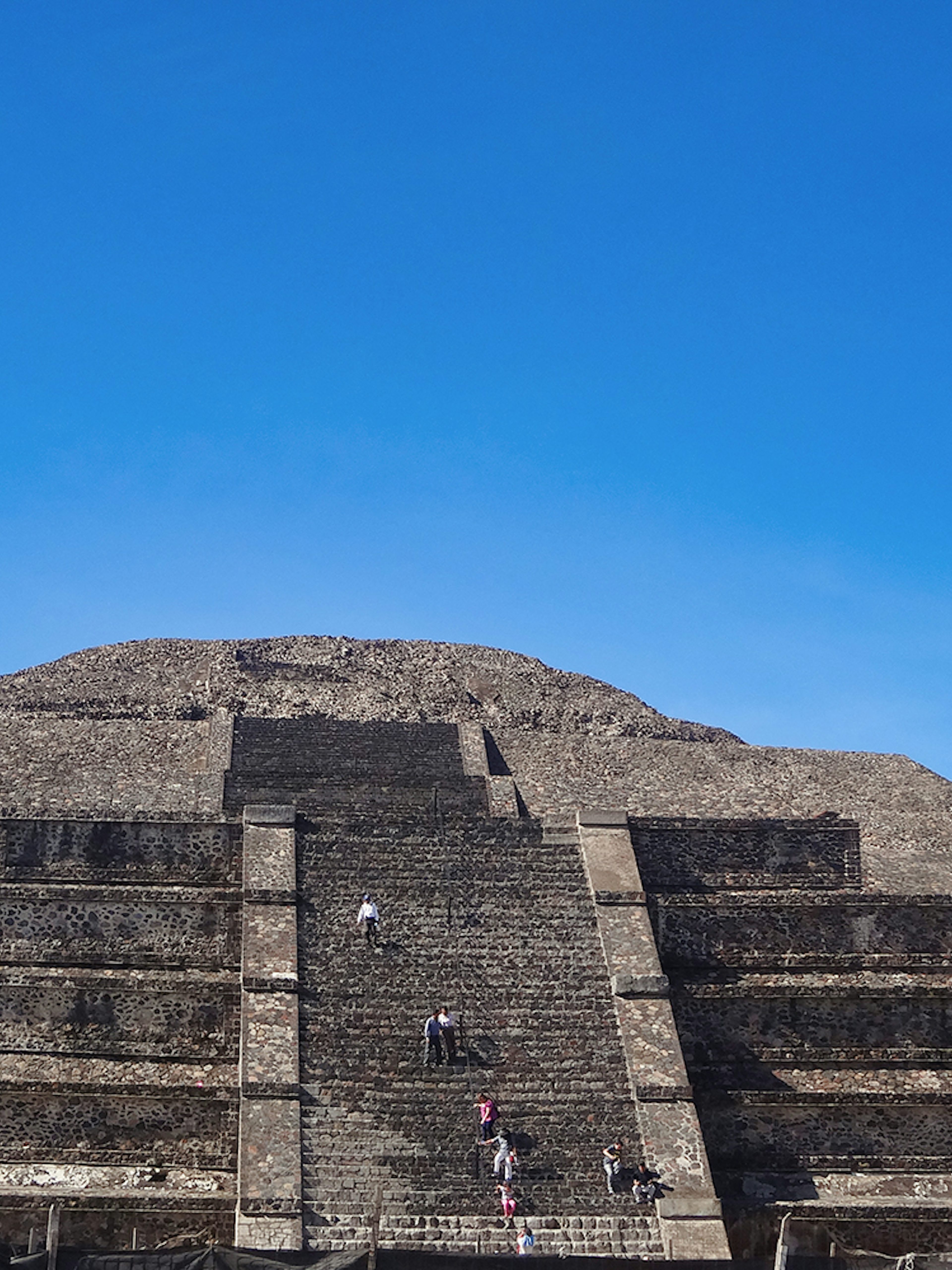 Visitors climbing the Pyramid of the Sun at Teotihuacan, Mexico under a clear blue sky.