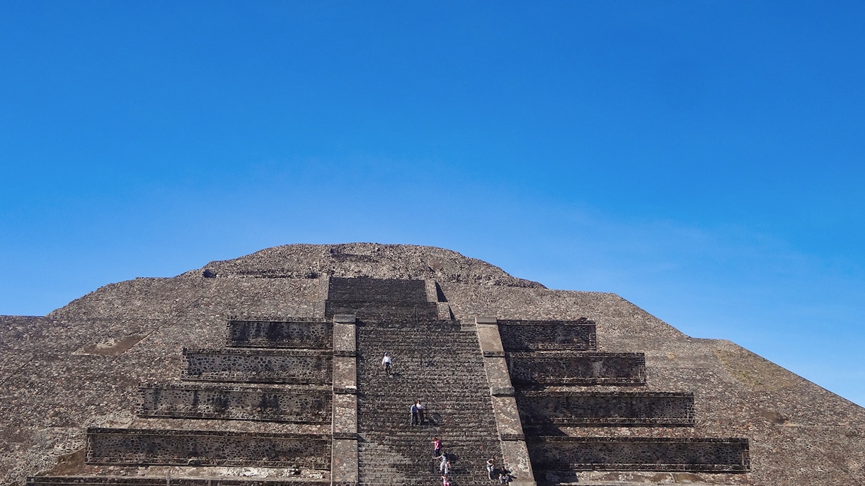 Visitors climbing the Pyramid of the Sun at Teotihuacan, Mexico under a clear blue sky.