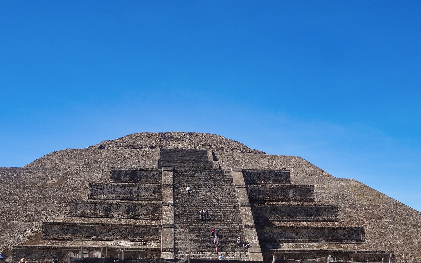 Visitors climbing the Pyramid of the Sun at Teotihuacan, Mexico under a clear blue sky.