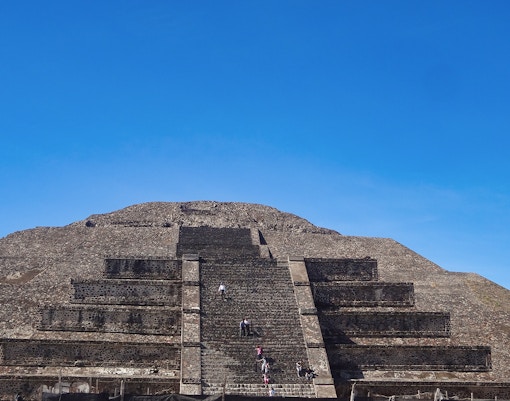 Visitors climbing the Pyramid of the Sun at Teotihuacan, Mexico under a clear blue sky.