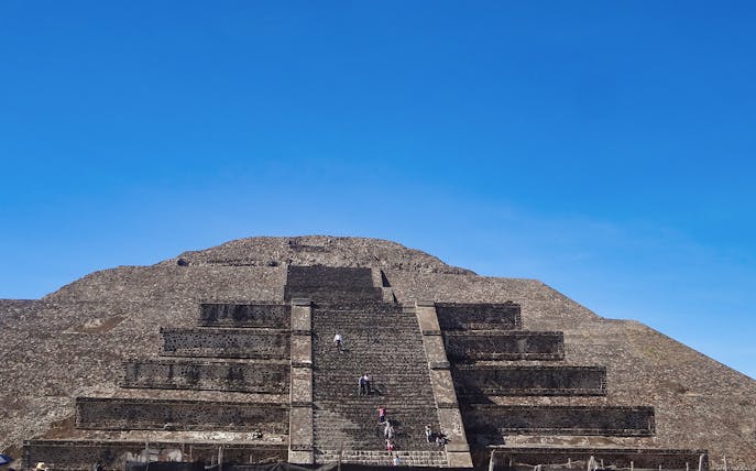 Visitors climbing the Pyramid of the Sun at Teotihuacan, Mexico under a clear blue sky.