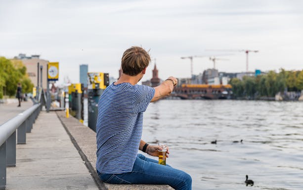 Man sitting by the Spree River in Berlin, pointing towards the Oberbaum Bridge.