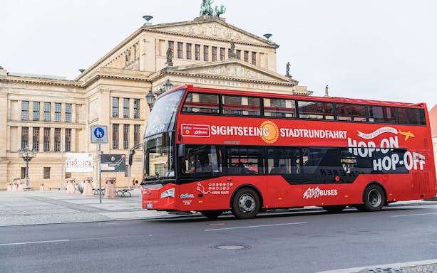 Red sightseeing bus in front of Konzerthaus Berlin for hop-on hop-off tour.
