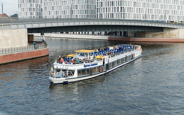 Cruise boat on the Spree River in Berlin passing under a modern bridge.