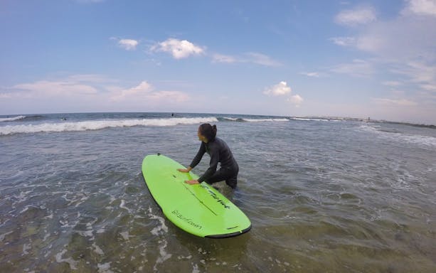Surfers riding waves in Chatan Town, Okinawa, with clear blue sea and distant coastline.