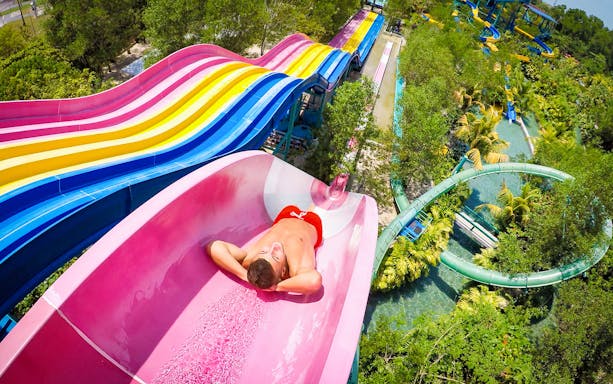 Person sliding down a colorful water slide at Escape Theme Park.