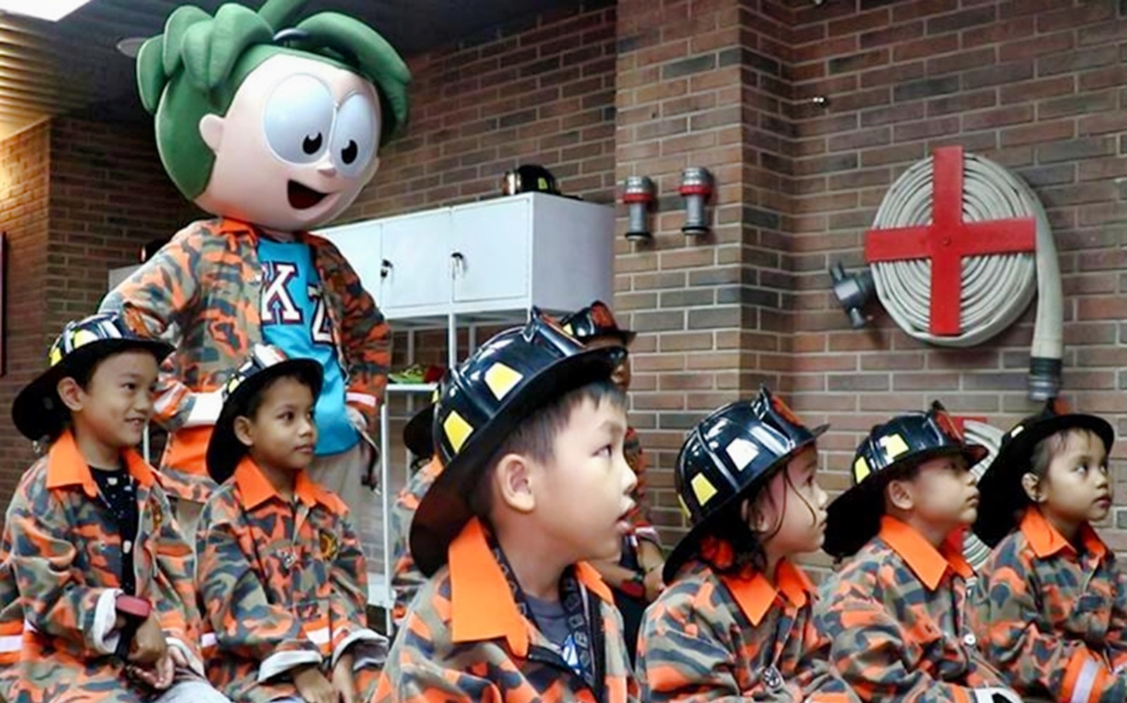 Children in firefighter uniforms at Kidzania Malaysia with a mascot.