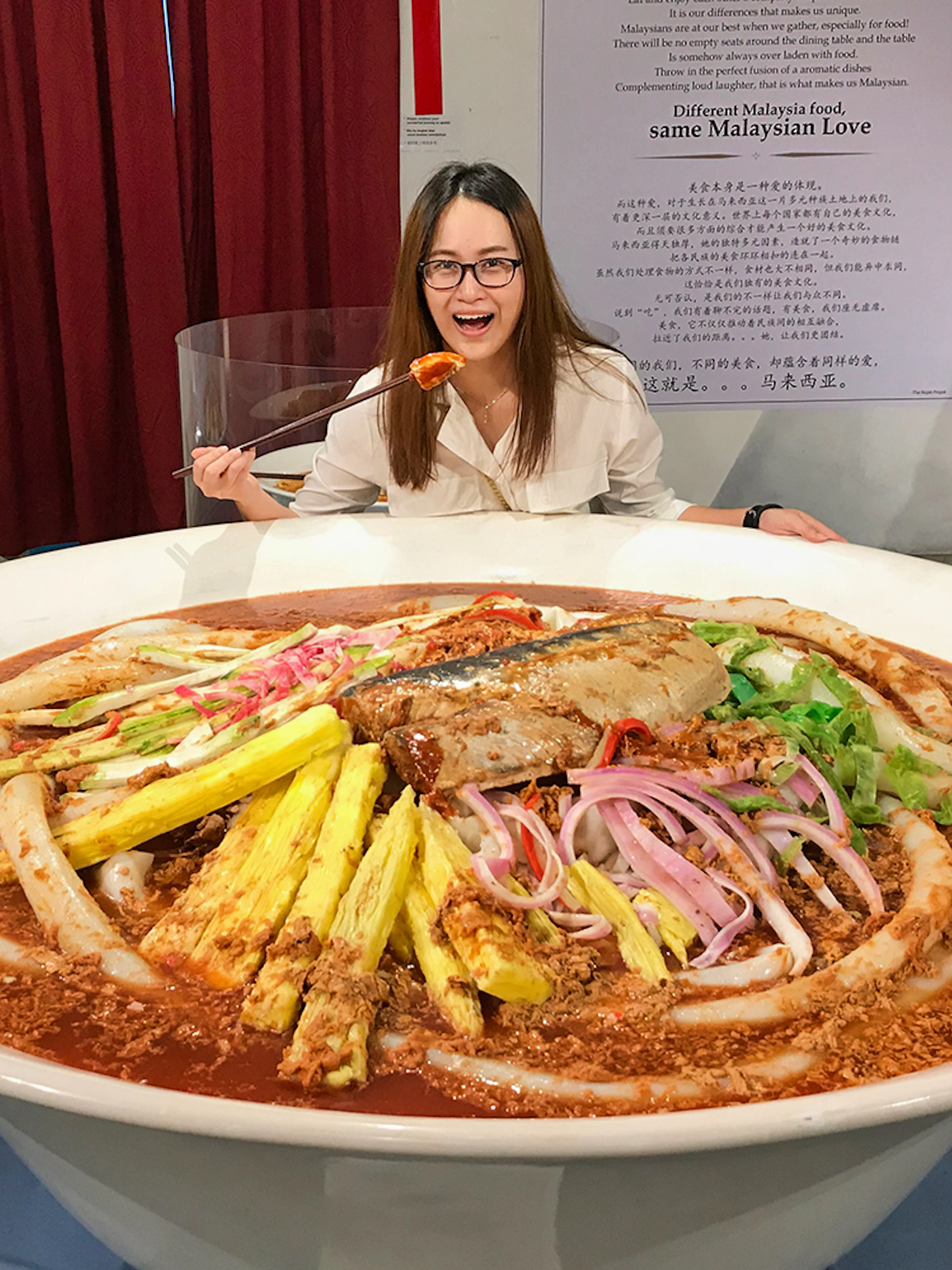 Giant bowl of Malaysian laksa at Wonderfood Museum, Penang, with a visitor posing.