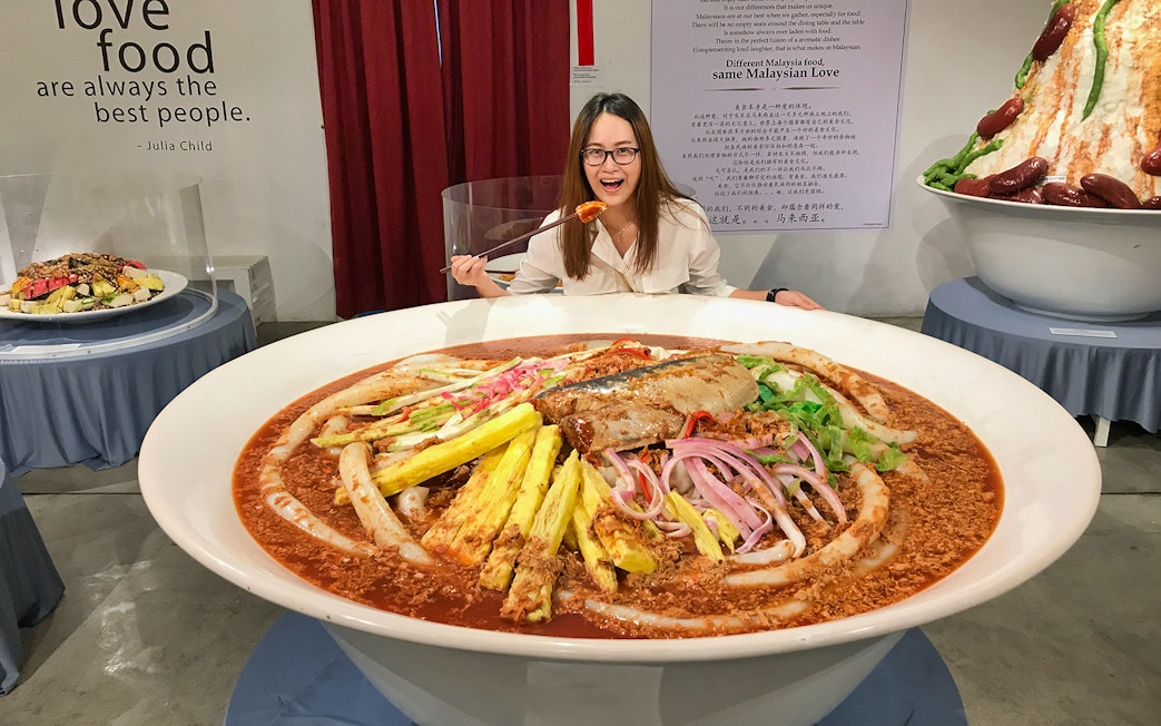 Giant bowl of Malaysian laksa at Wonderfood Museum, Penang, with a visitor posing.