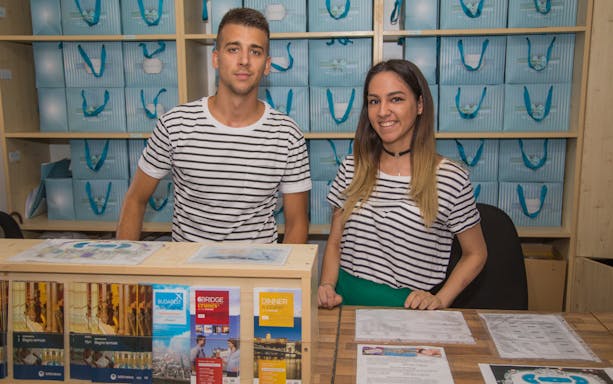 Staff at Széchenyi Spa reception desk with brochures for skip-the-line tickets and private cabin options.