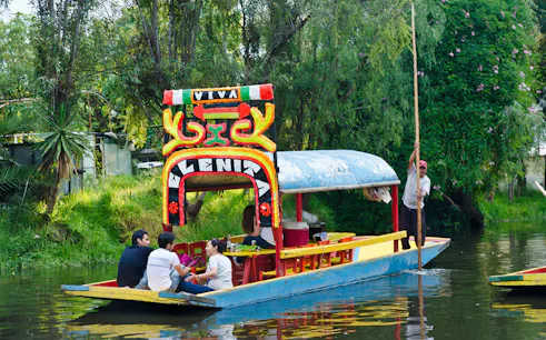 Colorful trajinera boat on Xochimilco canal, Mexico City, with people enjoying a guided tour.