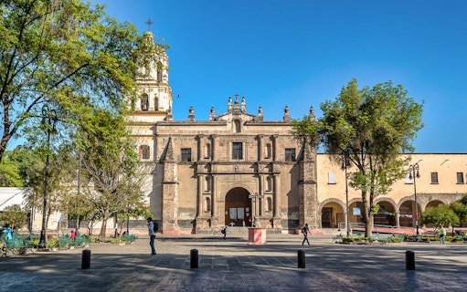 Historic church facade in Coyoacan, Mexico City, with people walking in the plaza.