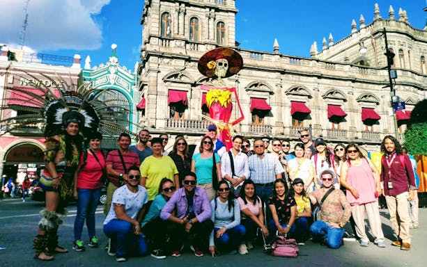 Group of tourists in front of Puebla's historic building with traditional dancer and skeleton figure.