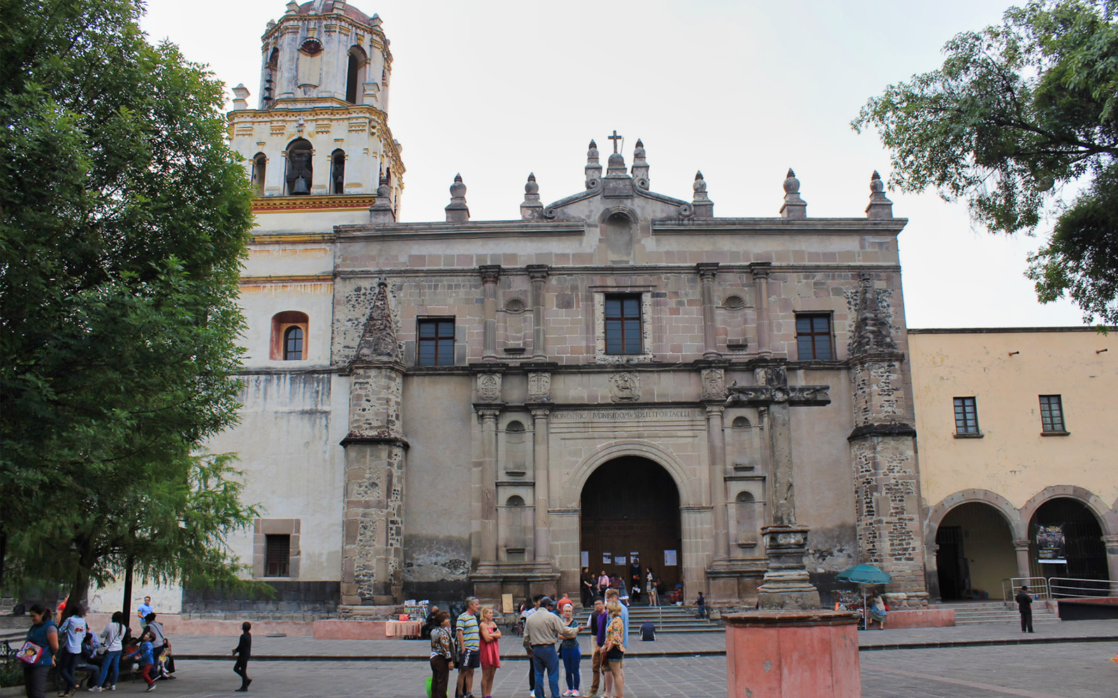 Church facade in Coyoacan, Mexico City, with tourists gathered in front.