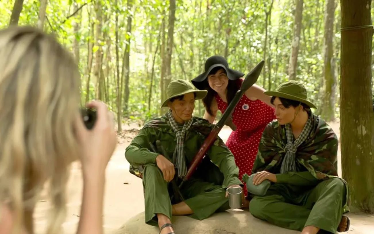Tourist posing with Cu Chi Tunnels mannequins in Ho Chi Minh City forest setting.
