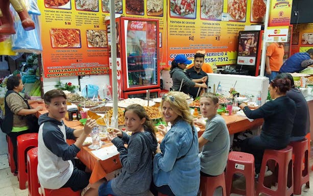 Visitors enjoying local cuisine at a bustling food market in Mexico City during the Xochimilco tour.