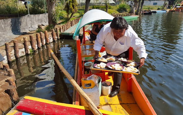 Man serving food on a colorful boat in Xochimilco, Mexico City canal.