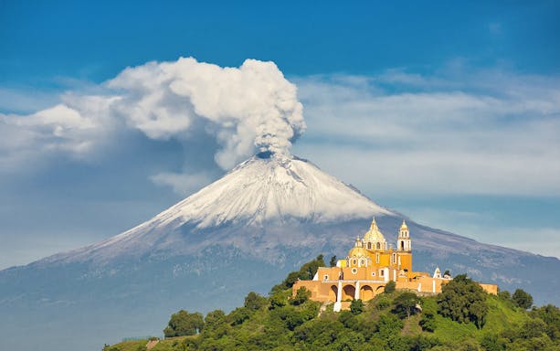 Popocatépetl volcano with smoke plume and Cholula church in Mexico City tour.