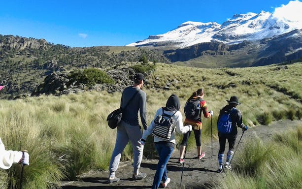 Hikers on a trail in Iztaccíhuatl-Popocatépetl National Park with snow-capped mountains in the background.