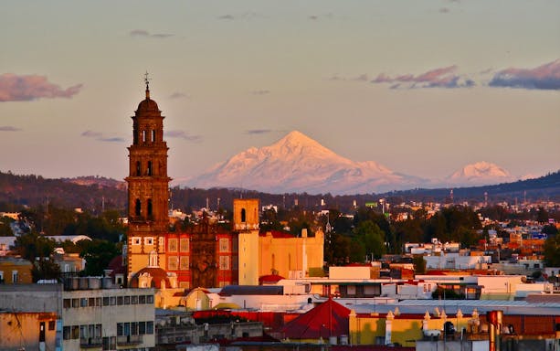 Iztaccíhuatl and Popocatépetl volcanoes viewed from a cityscape at sunset.