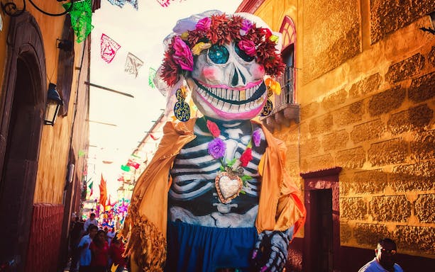 Giant skeleton figure in colorful attire during a festival in San Miguel de Allende.
