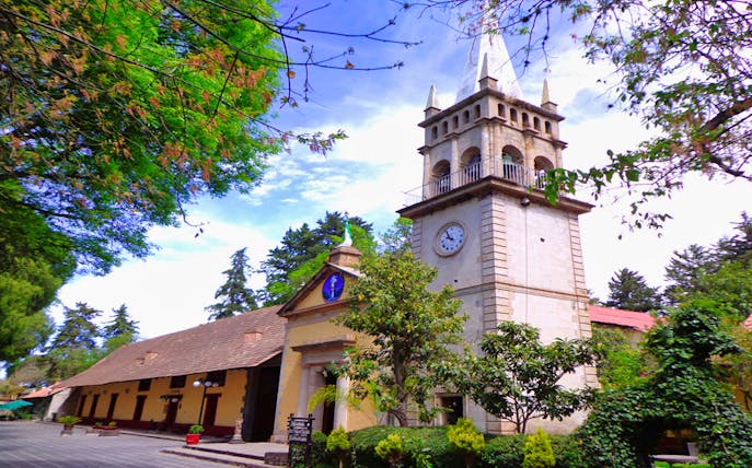 Clock tower and historic building in Real del Monte, Mexico, surrounded by lush greenery.