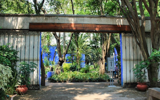 Entrance to Frida Kahlo Museum garden with lush greenery and exit sign, Mexico City.