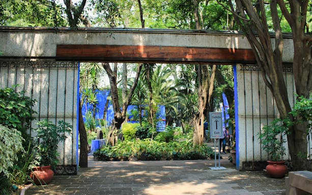 Entrance to Frida Kahlo Museum garden with lush greenery and exit sign, Mexico City.