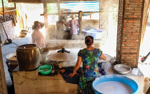 Locals making rice paper in a traditional workshop during Mekong Delta tour.