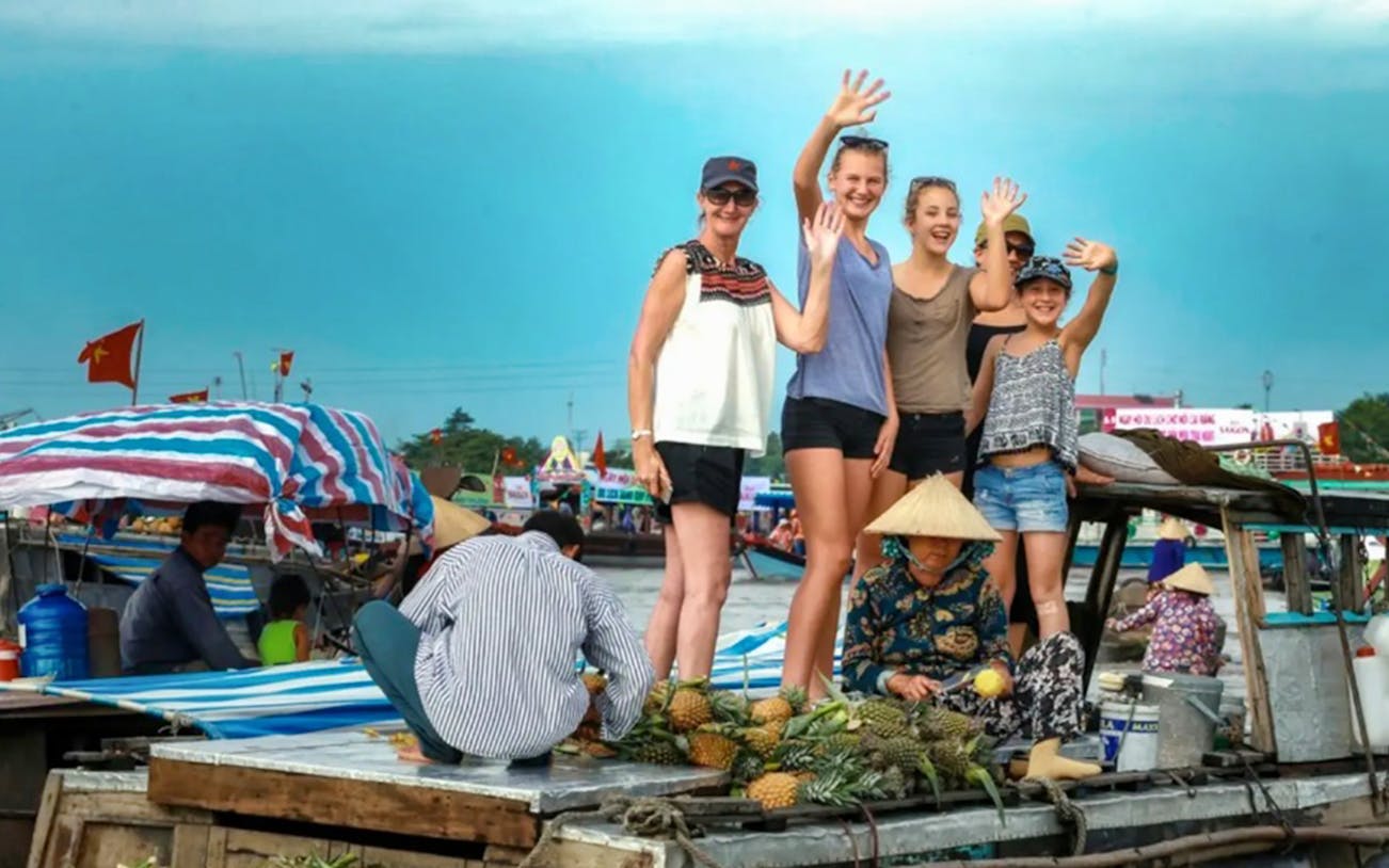 Tourists waving on a boat at the Mekong Delta floating market.