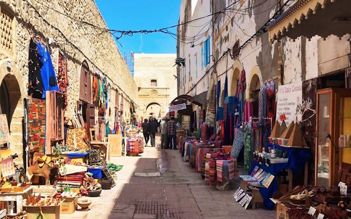 Essaouira Medina market street with colorful textiles and crafts, Morocco.