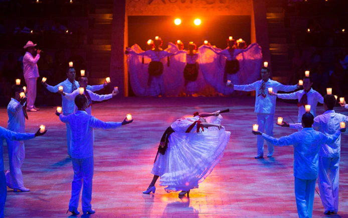 Dancers performing traditional Mexican dance with candles at Xcaret Park night show.