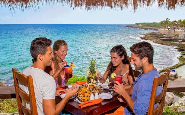Dining by the ocean at Xcaret Park, Mexico, with tropical drinks and a pineapple centerpiece.