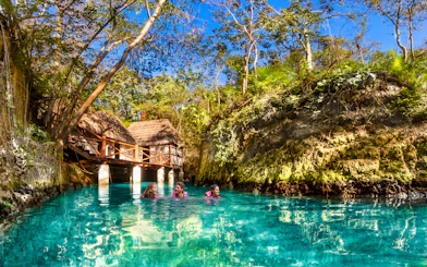 Visitors swimming in a turquoise river surrounded by lush greenery at Xcaret Park, Mexico.
