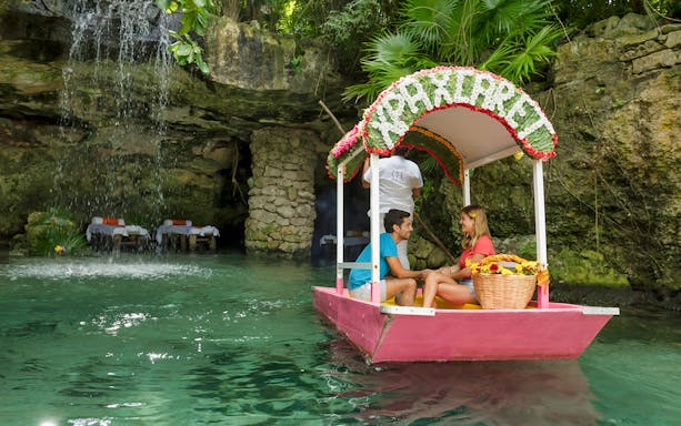 Couple on a boat tour at Xcaret Park with waterfall and spa area in the background.