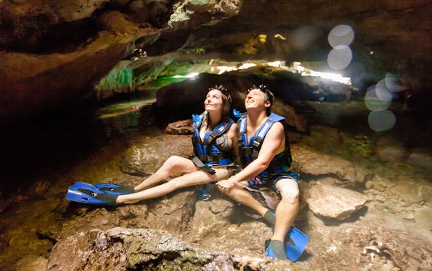 Visitors exploring a cave at Xel Há Park, wearing life vests and flippers.