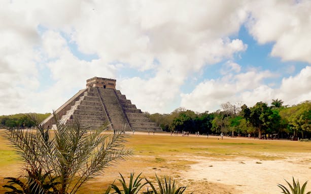 Chichen Itza pyramid under a cloudy sky, surrounded by greenery, Yucatán, Mexico.