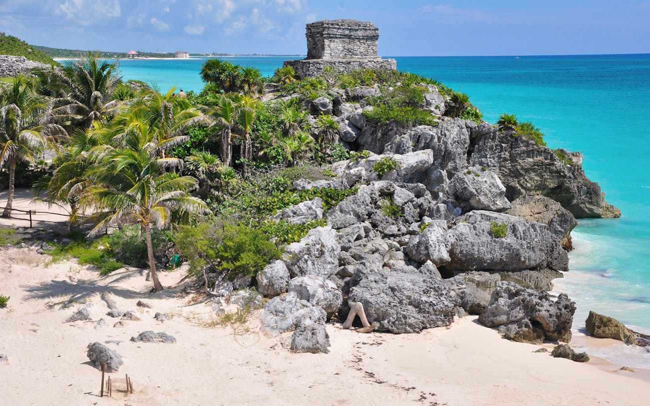 Tulum ruins overlooking the Caribbean Sea with palm trees and rocky cliffs.
