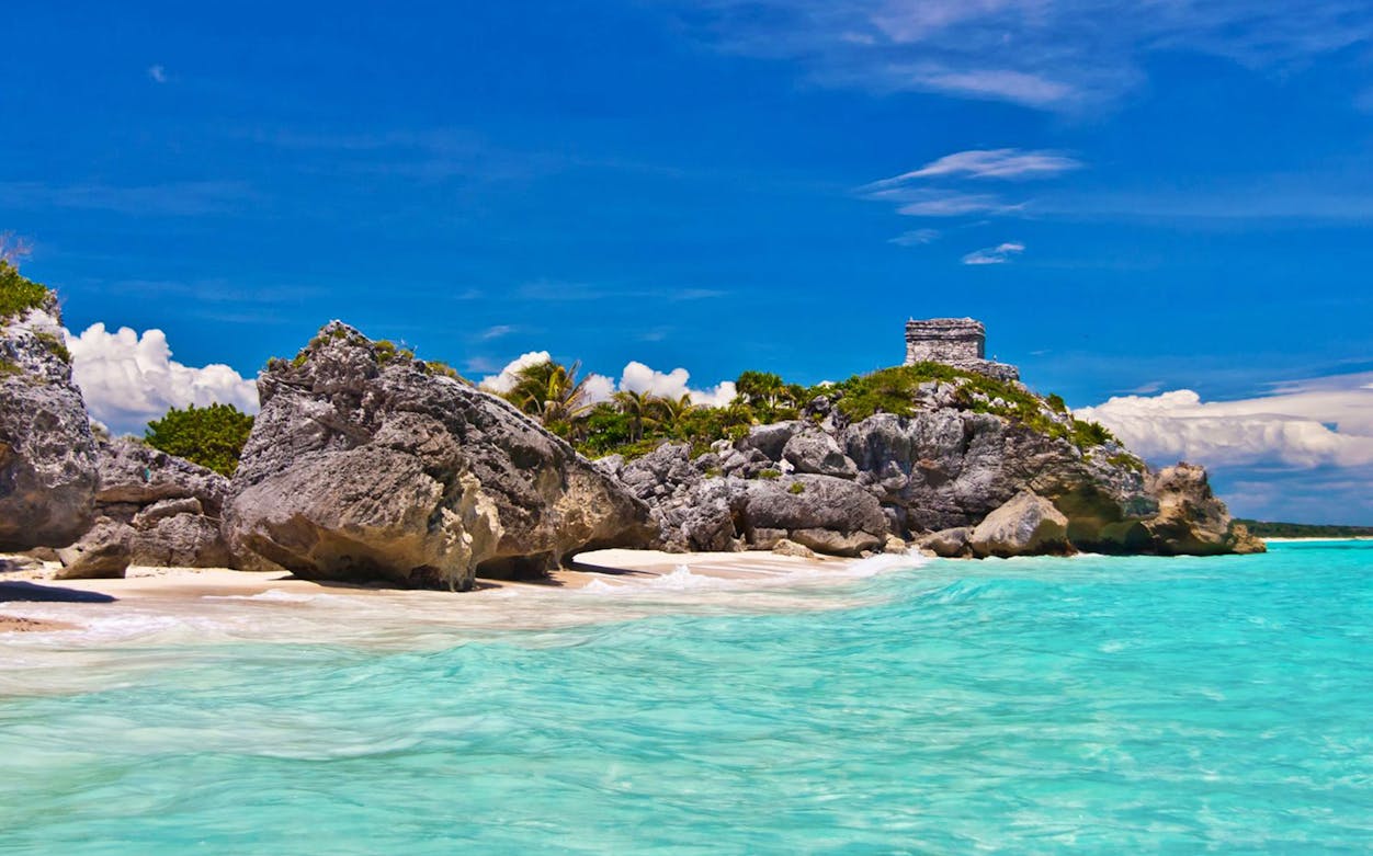 Tulum ruins overlooking turquoise sea and rocky beach.
