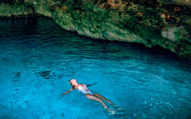 Person floating in a clear blue cenote cave during Tulum Mayan Ruins & Dos Cenotes Tour.