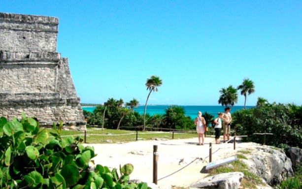 Tulum Mayan ruins with tourists overlooking the Caribbean Sea.