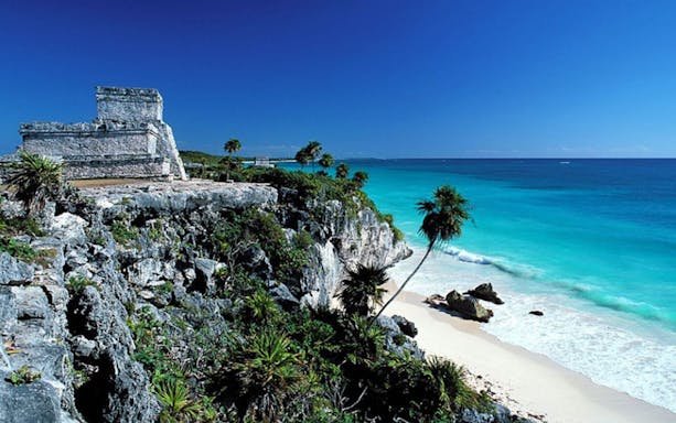 Tulum Mayan Ruins overlooking the Caribbean Sea with palm trees and rocky cliffs.