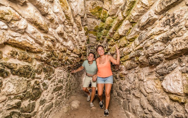 Tourists exploring a stone tunnel in Coba Maya Village, Mexico.
