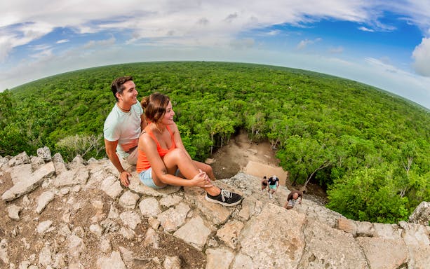 Visitors sitting atop Coba pyramid overlooking lush jungle, Tulum & Coba Maya Village tour.