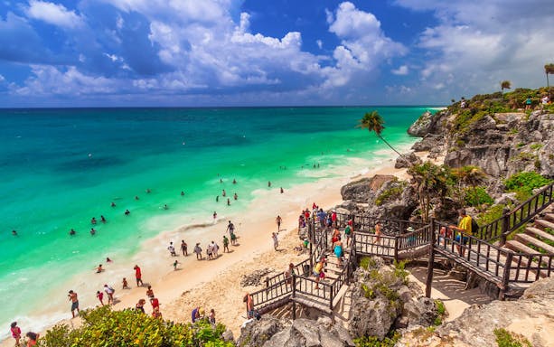 Visitors exploring Tulum Ruins beach with turquoise water, part of the Cancun half-day tour.
