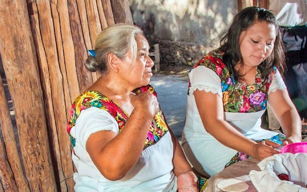 Women in traditional attire crafting pottery in a Mayan village during Coba bike tour.