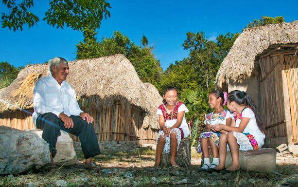 Elder and children in traditional attire outside Mayan huts in Coba village.